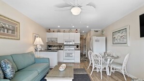 Un espace de vie compact comprenant un canapé, une table basse, une table à manger et des chaises. On peut apercevoir une kitchenette équipée d’un four à micro-ondes, d’un four et d’un réfrigérateur.