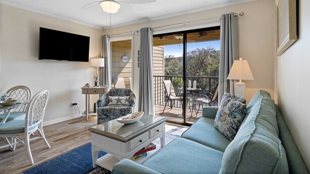Un salon comprenant un canapé, des fauteuils, une table basse, un téléviseur et un balcon aménagé avec du mobilier d’extérieur.