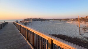 Une promenade en bois mène à une plage de sable fin, sous un ciel dégagé.