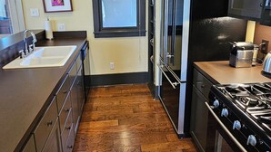 Una cocina con piso de madera, electrodomésticos de acero inoxidable y un ventanal con adornos rojos.