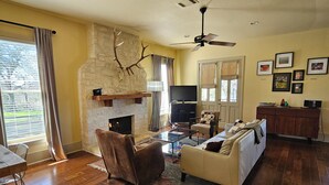 Una sala de estar con chimenea de piedra, ventilador de techo, televisor, sofá y comedor con mesa y sillas.