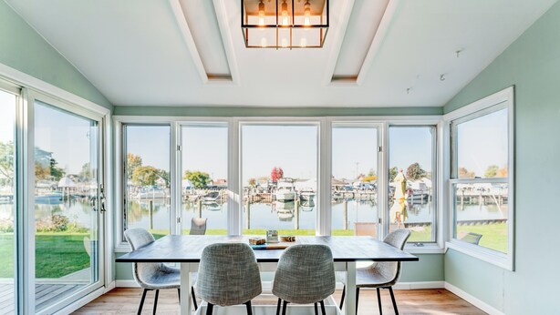 Un comedor con mesa y sillas, ventanas amplias y vista hacia un puerto deportivo.