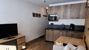 A modern living room with a sofa, a coffee table, and a TV. There is a kitchen area with wooden cabinets and a microwave. - Ski-in/ski-out & foot of the slopes, 2nd floor, view ski slopes, balcony, tv, 20m², La Plagne (La Plagne)