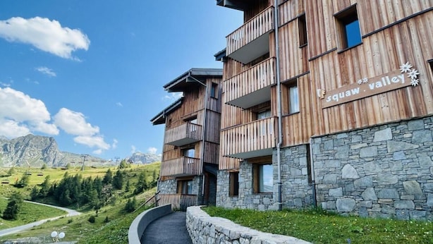 Ein Holzgebäude mit Balkonen und einem Steinsockel, beschriftet mit „Squaw Valley“.