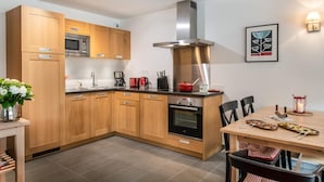 Une cuisine moderne avec des meubles en bois, des appareils en acier inoxydable et un coin repas comprenant une table et des chaises.