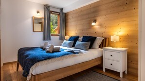 Une chambre à coucher avec une tête de lit en bois, une table de chevet blanche, un grand lit avec une literie bleue et blanche, une fenêtre avec des rideaux et un luminaire fixé au mur.
