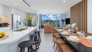 Une cuisine moderne dotée d’un îlot central, de tabourets de bar et d’un coin repas avec une longue table pouvant accueillir six personnes.