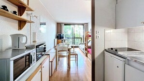 A compact kitchen with a microwave, stove, and sink. There is a dining table with chairs and a window providing a view of the outdoors. - 2nd floor, view mountain, swimming pool, balcony, tv, ski locker, 21m², Le Corbier (Le Corbier)