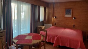 A wooden-paneled room with a bed, a table with chairs, and a window with curtains. - 100m from resort center, 3rd floor, balcony, tv, ski locker, 30m², Brides Les Bains (Brides-les-Bains)