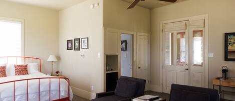 A bedroom with a red metal bed frame, a ceiling fan, and a door leading to a bathroom.