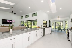 A modern kitchen with white cabinetry, a marble countertop, and a large window overlooking a garden. - Enchanting 2.5-acre Naples Estate. 20min drive to beach. Sleeps 8.  AC/WiFi/Pets (Naples)