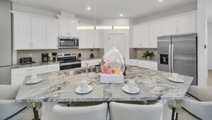 Una cocina moderna con armarios blancos, una isla central con cúpula de cristal, electrodomésticos de acero inoxidable y encimeras de mármol.