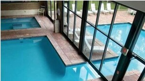 An indoor swimming pool with clear glass walls, a diving board, and a tiled floor marked with depth indicators.