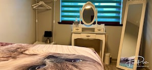 A bedroom with a bed, a dresser with a mirror, a lamp, and a window with blinds. - Luxurious and Cozy Apartment (Dundee)