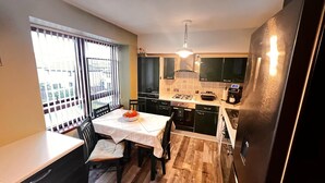 Cocina compacta con una mesa, sillas, una ventana con persianas y electrodomésticos modernos.