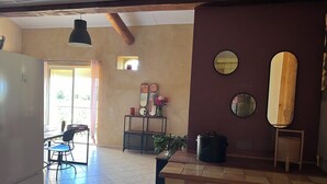 Una cucina con pavimento piastrellato, un'area pranzo con tavolo e sedie, e un'ampia finestra che fa entrare luce naturale.
