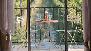 Un balcone con un tavolo apparecchiato per due persone, una bottiglia di liquore e due bicchieri. Si intravede una vigna e una collina in lontananza.
