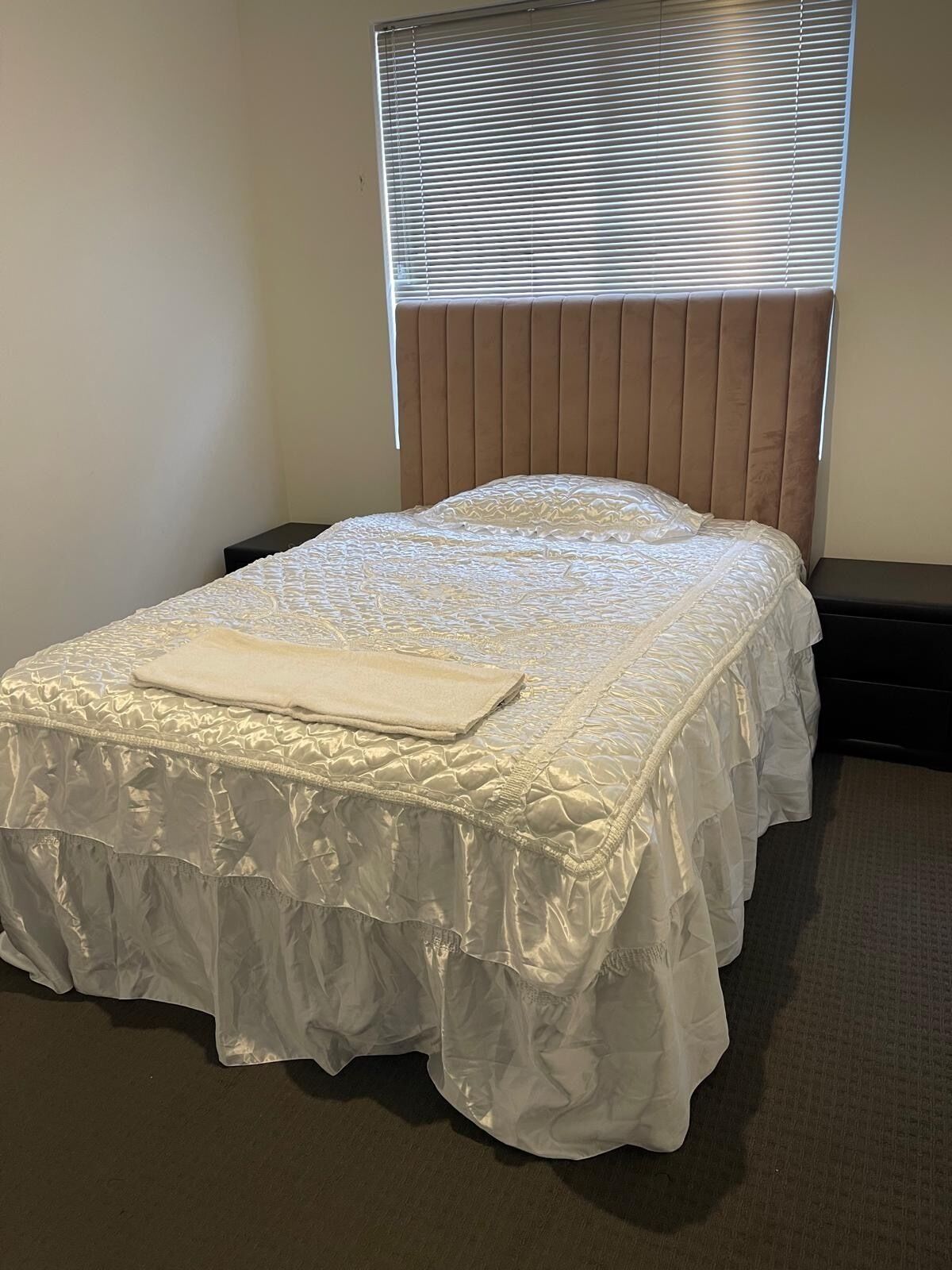 A neatly made bed with a white bedspread and a folded blanket on top, positioned in a room with a window and a wooden headboard.