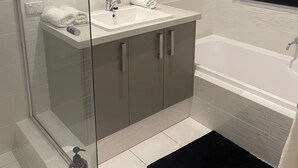 Un baño moderno con cabina de ducha de vidrio, un lavabo blanco con espejo y una bañera.