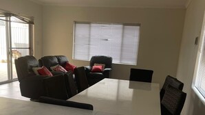 Una sala de estar moderna con un conjunto de sofá, una mesa de comedor y un amplio ventanal con persianas.