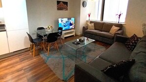 A modern living room with a glass coffee table, a sofa, a TV, and a dining area with chairs and a small table. - Broad St - 1 Bedroom - 1 Bathroom - Free Parking (Birmingham)