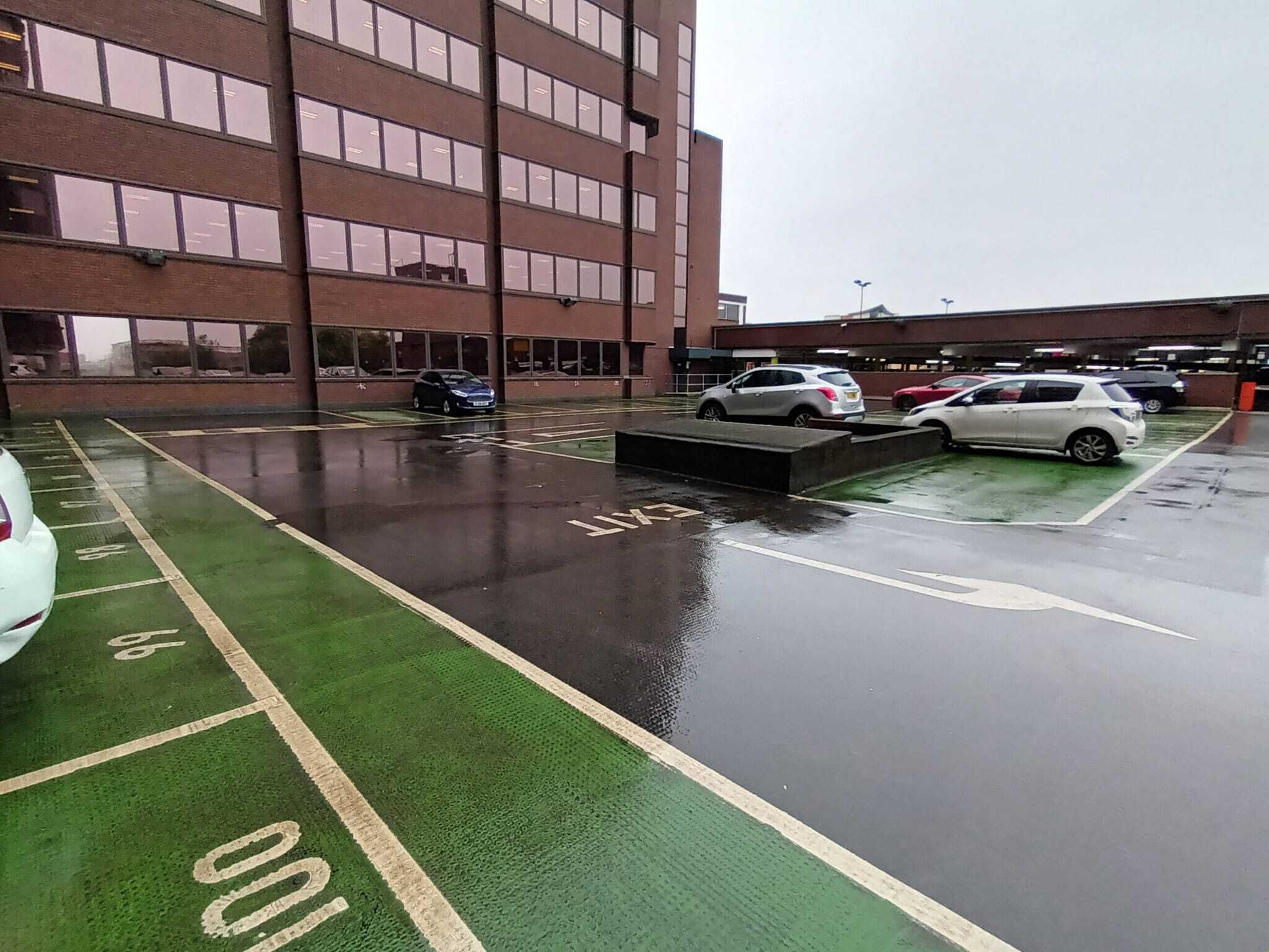 A parking lot with marked spaces, a building with multiple floors, and a wet ground surface.