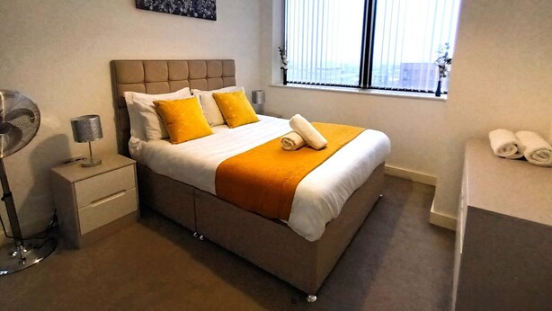 A modern hotel room with a large bed, a bedside table with a lamp, a window with blinds, and a painting on the wall. - Broad St - 1 Bedroom - 1 Bathroom - Free Parking (Birmingham)