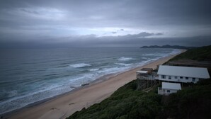 Vista costera con playa, olas del océano y un edificio de techo blanco.