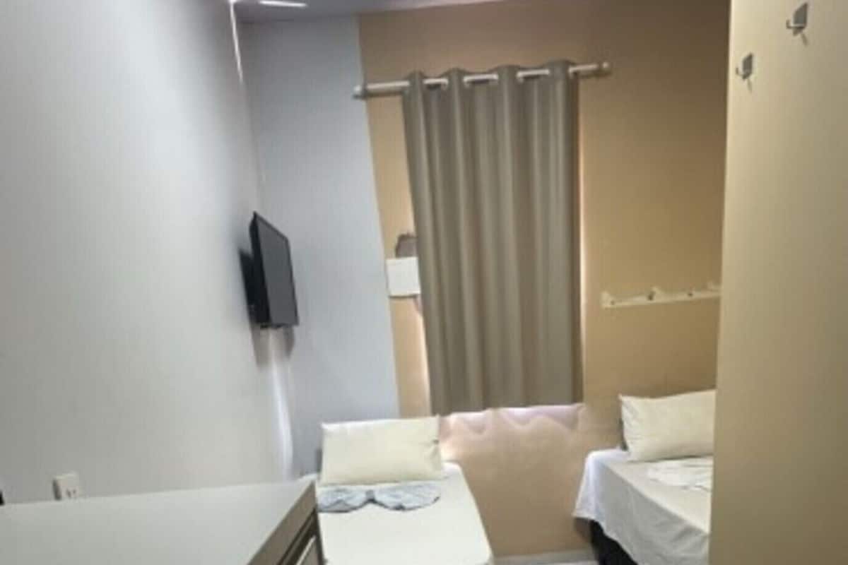 Une petite chambre propre, avec un lit, un bureau et un téléviseur fixé au mur.