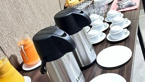 A breakfast setup with coffee makers, cups, and a basket of bananas on a wooden table. - Hotel Porto Sollar (Porto Nacional)