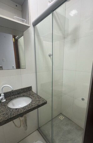 A bathroom with a granite countertop sink, a glass shower enclosure, and white tiled walls. - Hotel Porto Sollar (Porto Nacional)