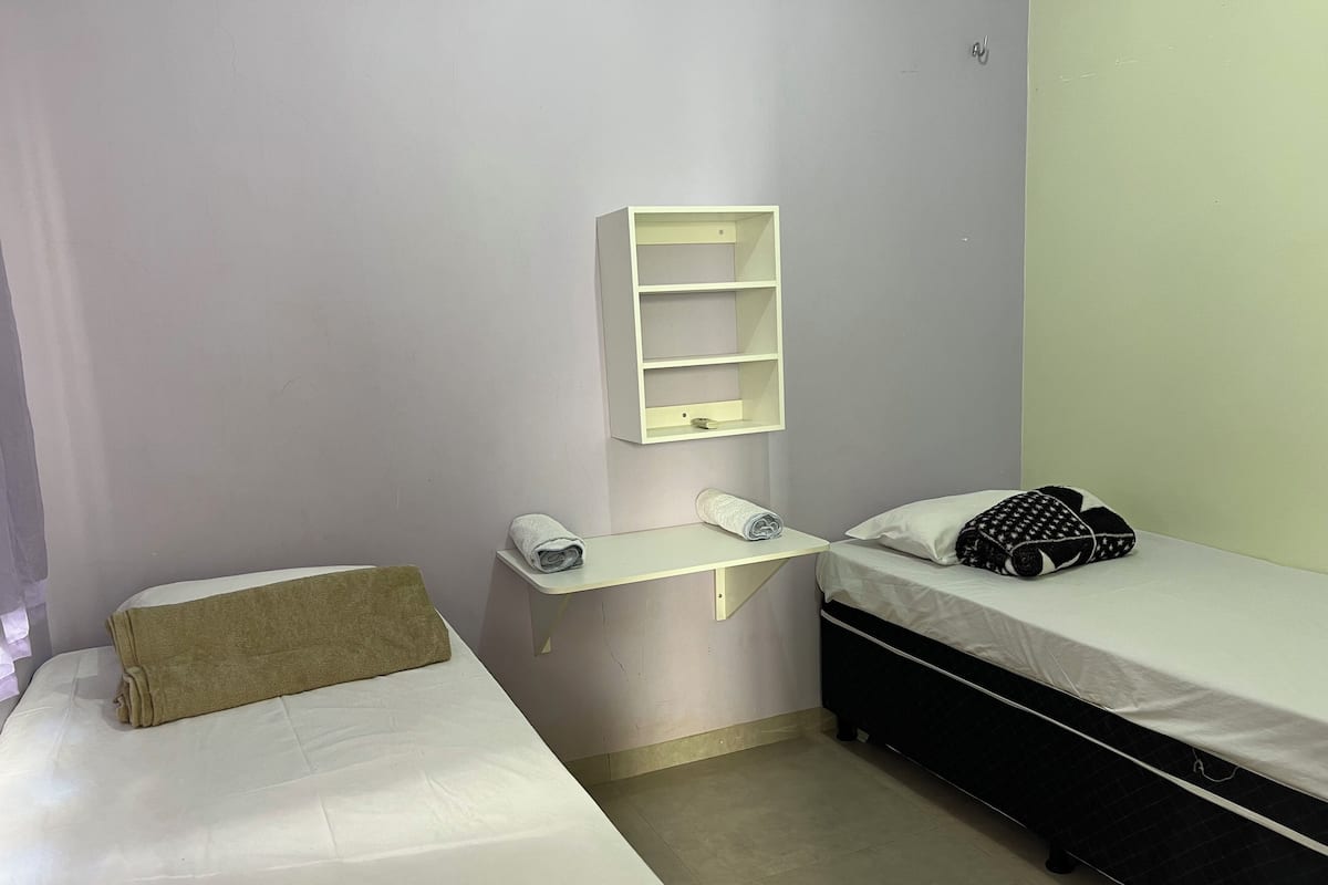 Une chambre avec deux lits, une petite étagère blanche et une serviette sur le lit situé à gauche.