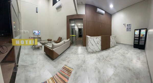 A hotel lobby with a sofa, a small table, a TV, a reception desk, and a vending machine. - Hotel Porto Sollar (Porto Nacional)