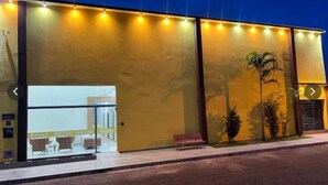 A hotel with a yellow facade, a glass entrance, and a bench outside. - Hotel Porto Sollar (Porto Nacional)