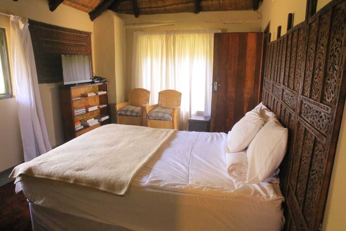 A bedroom with a bed, two chairs, a wooden wardrobe, and a window with curtains.