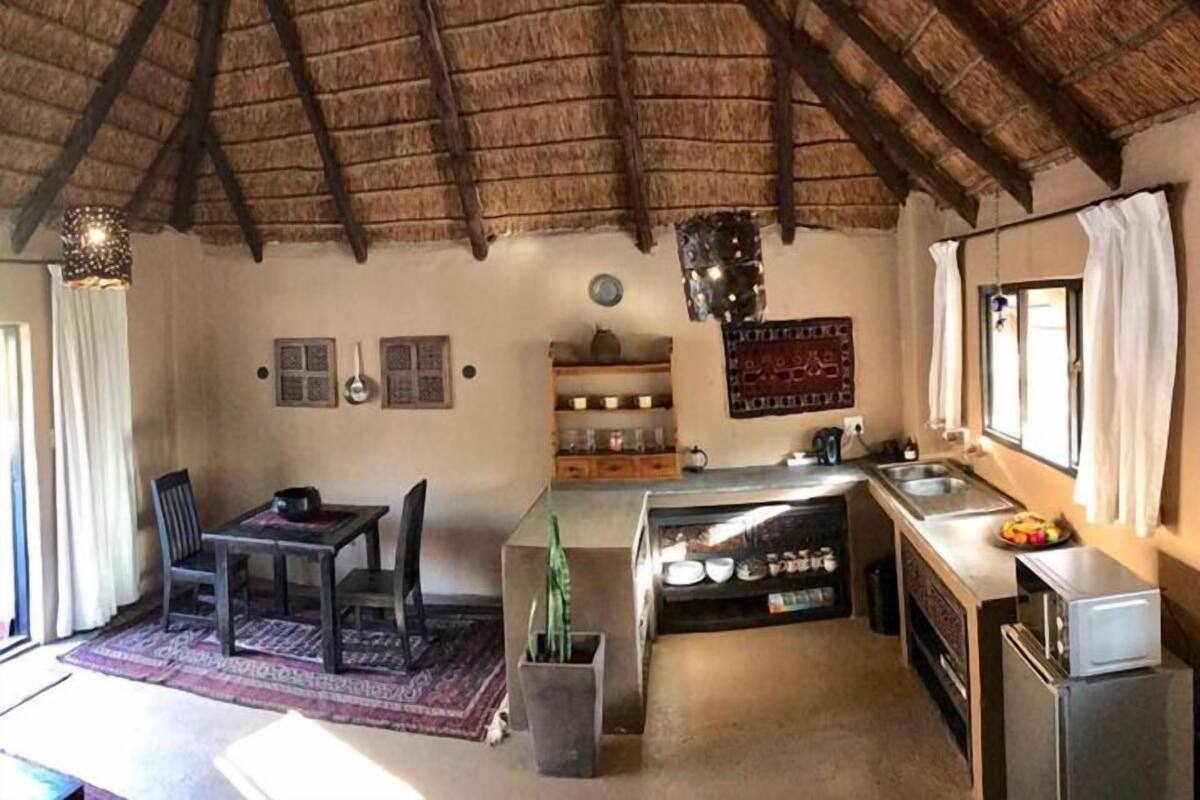 A compact kitchen with a rustic thatched ceiling, a dining area with chairs, and a small refrigerator.