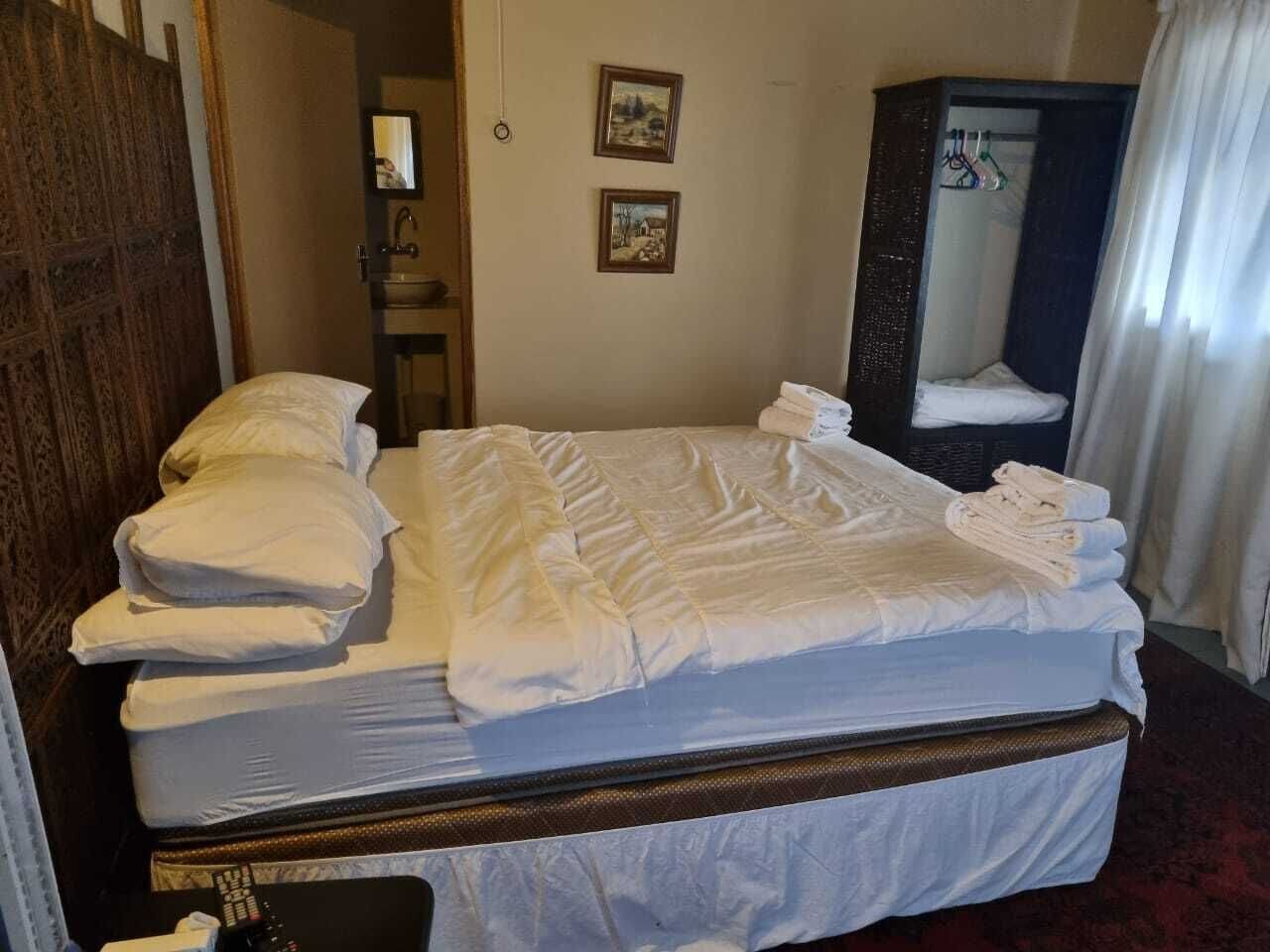 A neatly made bed with pillows, a wooden headboard, a mirror, and two framed pictures on the wall.