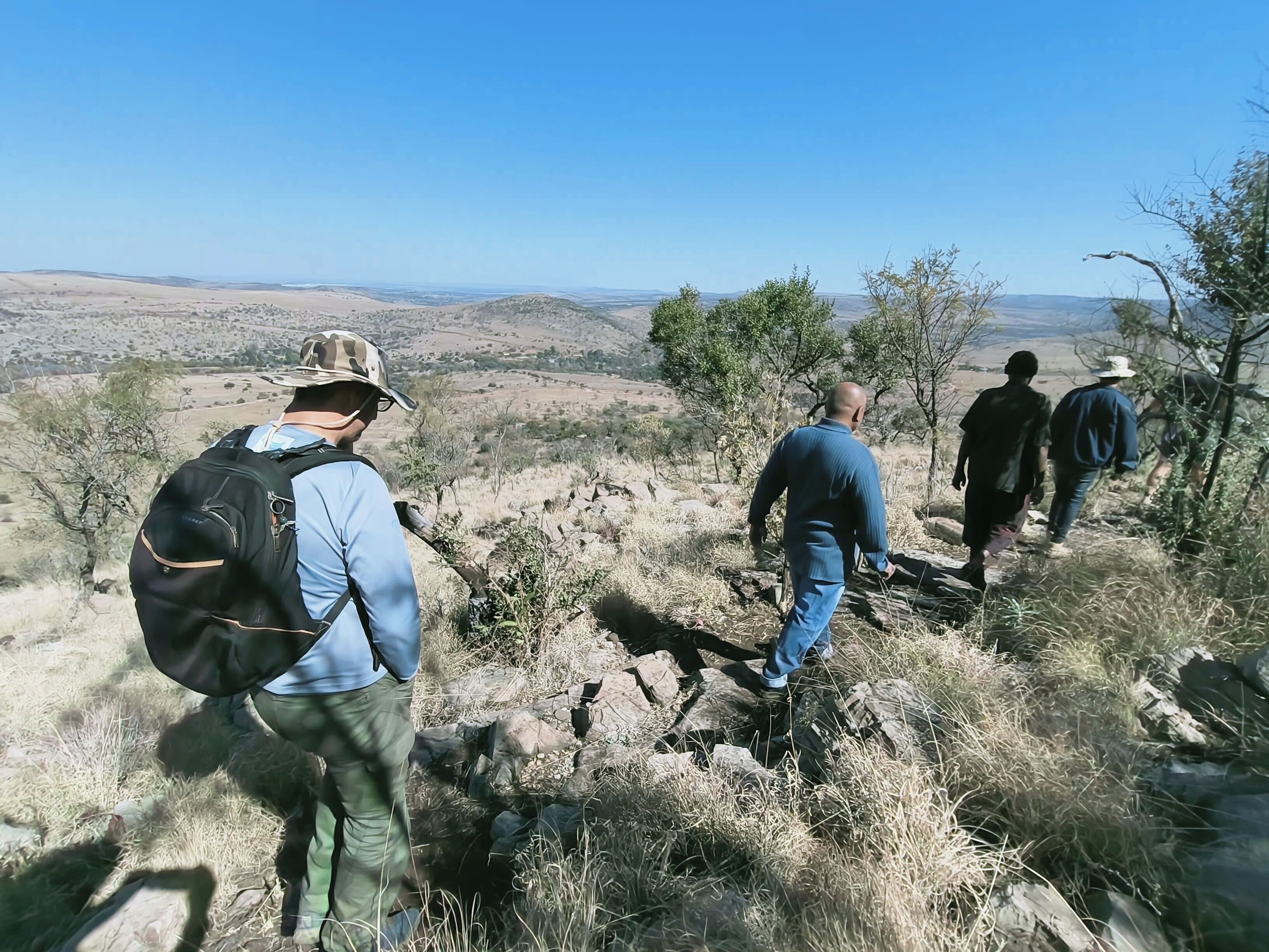 Un grupo de excursionistas en un sendero pedregoso, con vistas a colinas distantes.