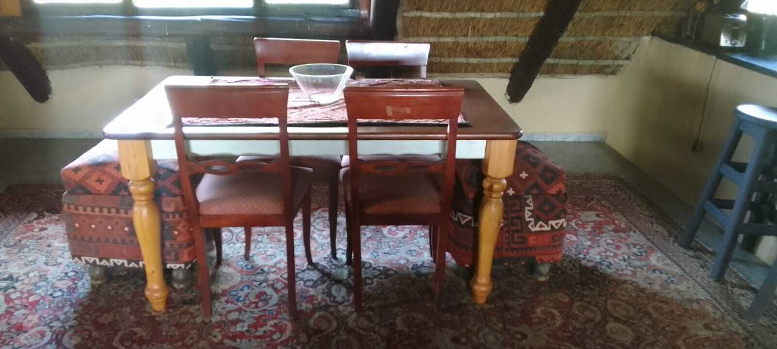 Ein Essbereich mit Holztisch und Stühlen, einem gemusterten Teppich und einem blauen Hocker.