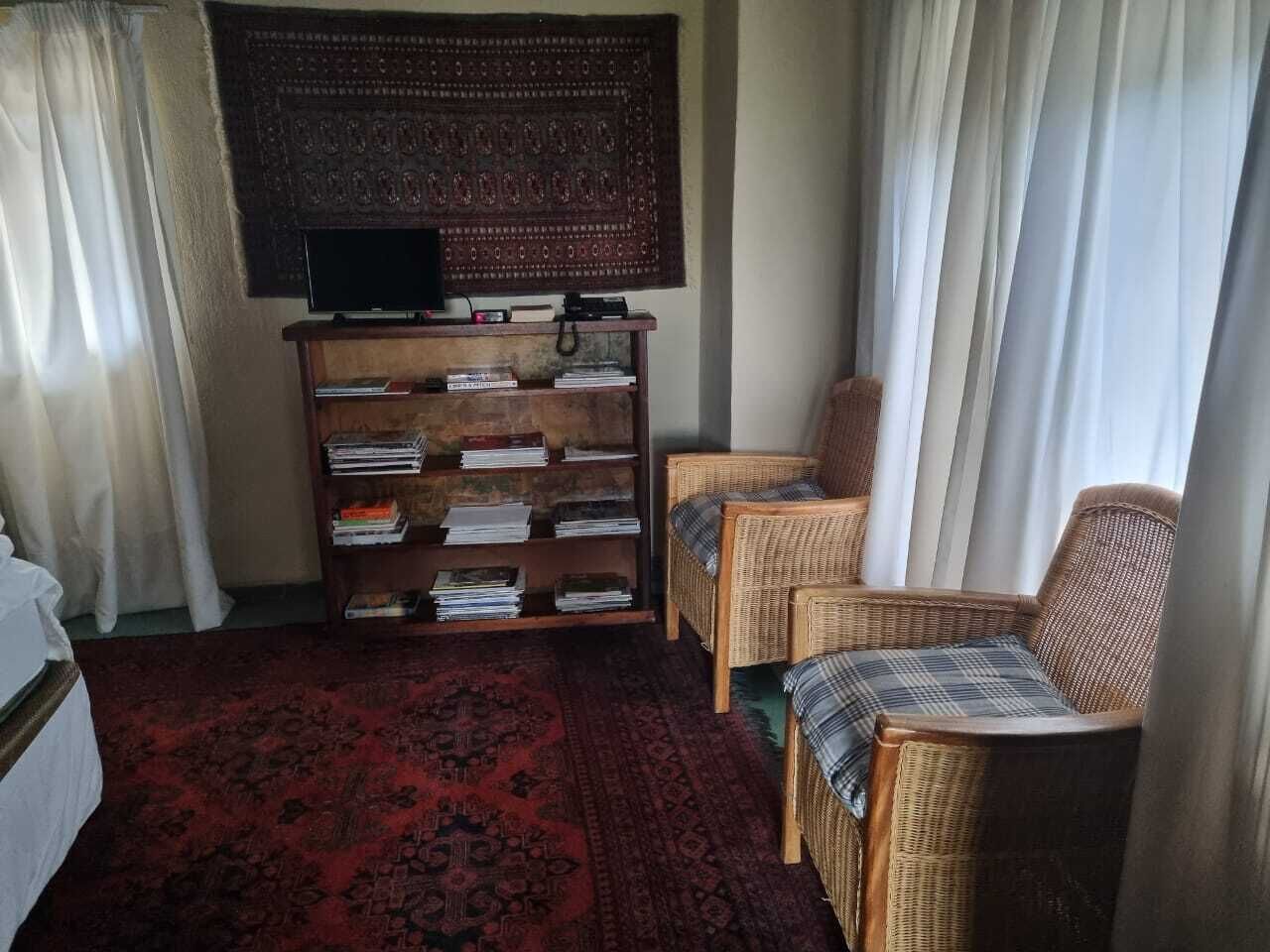 A room with a television on a wooden stand, a bookshelf, two wicker chairs, and a red patterned carpet.