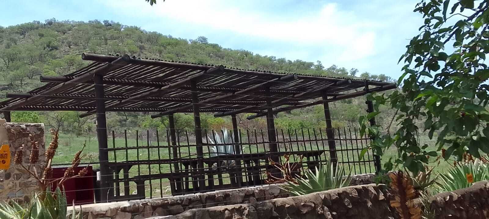 Una pérgola de madera con cerramiento de metal en un entorno natural.