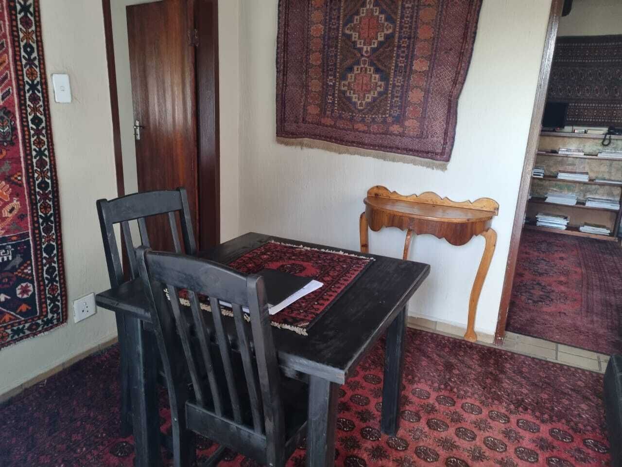 Una habitació amb una taula de fusta i cadires, una petita taula auxiliar de fusta i una catifa amb dibuixos al terra.