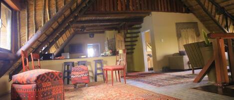 Um quarto de sótão acolhedor com teto inclinado, sala de jantar com mesa e cadeiras, e cozinha com balcão e banquetas.