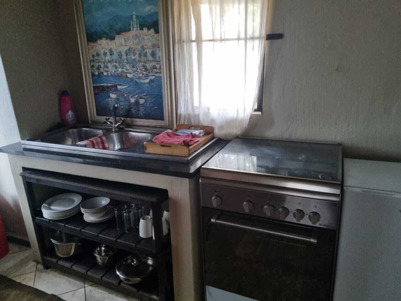 Cocina pequeña con pileta, estufa y estantes para vajilla.