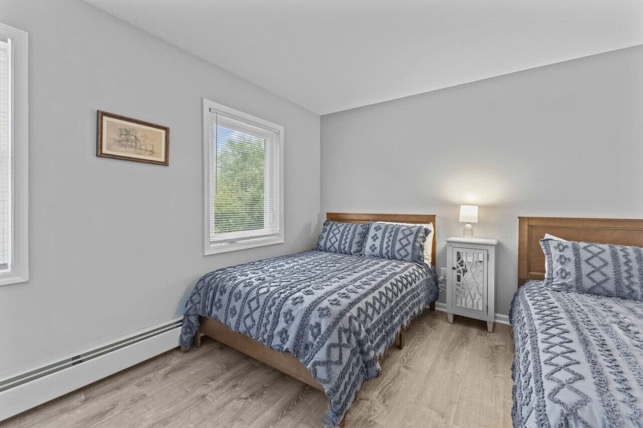 A bedroom with two beds, a nightstand, a framed picture, and a window with blinds.