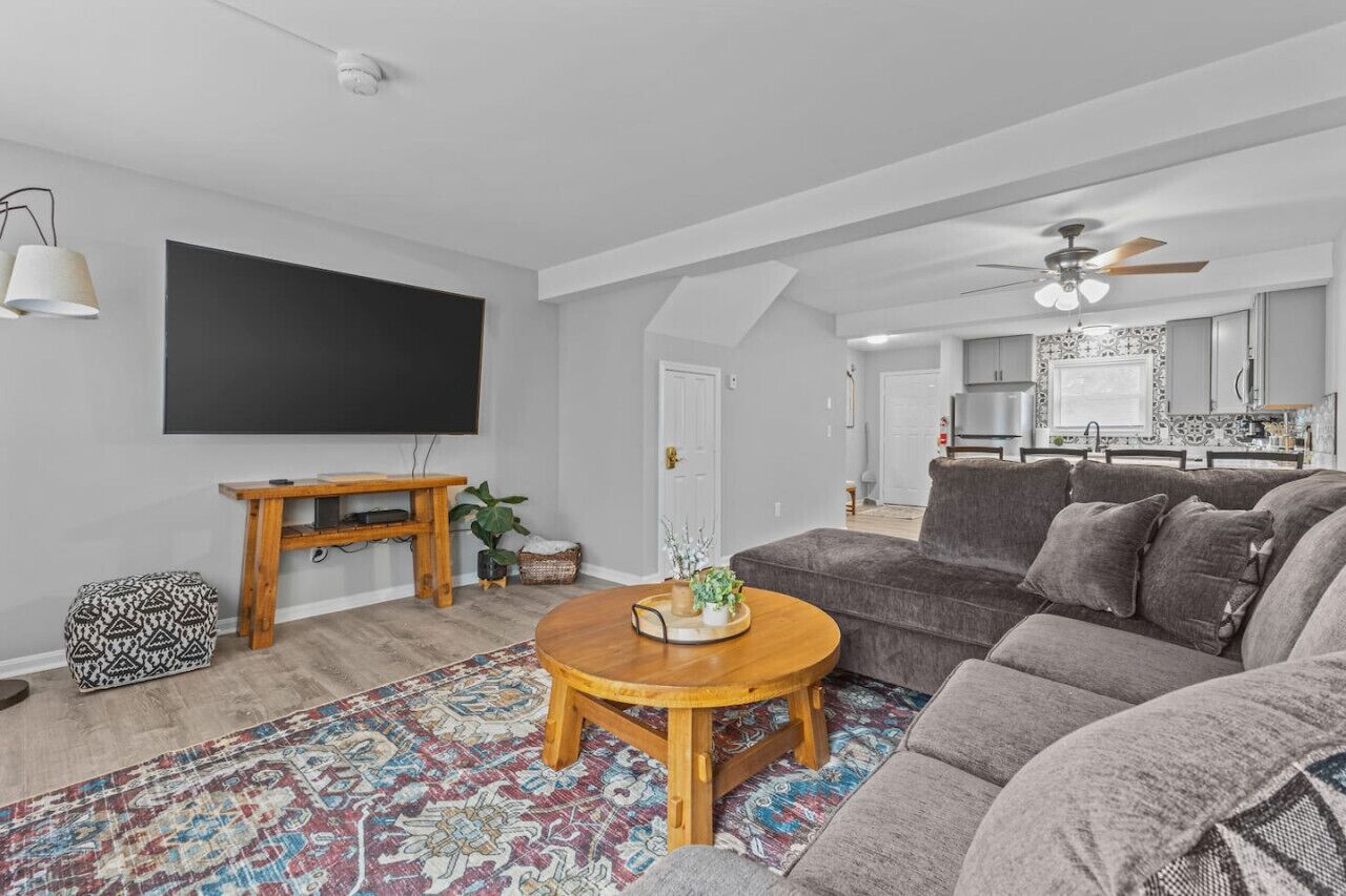 Una sala de estar moderna con un sofá gris, una mesa de centro de madera y una alfombra estampada.