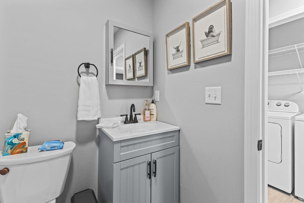 Un bagno con WC, lavandino e specchio. Alle pareti si notano quadri incorniciati, un asciugamano appeso e una saponetta sul lavandino.