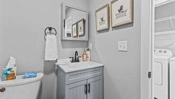 Un bagno con WC, lavandino e specchio. Alle pareti si notano quadri incorniciati, un asciugamano appeso e una saponetta sul lavandino.