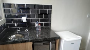 A compact kitchen with a granite countertop, a built-in microwave, a sink, and a white refrigerator.