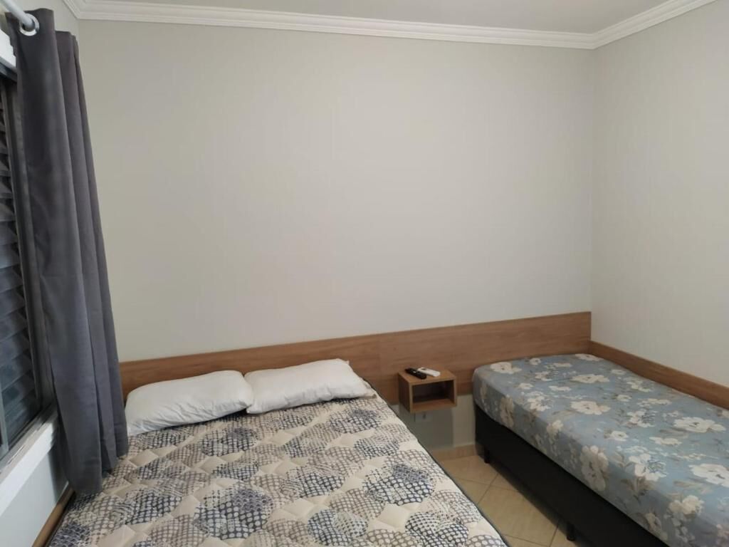 Quarto com duas camas, uma mesinha de cabeceira e uma janela com cortinas.